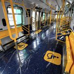 Interior of the new subway car, which has yellow poles, railings, hand holds, and fold down seats. THe regular seats are blue. There's also plastic on the floor to protect it for now.